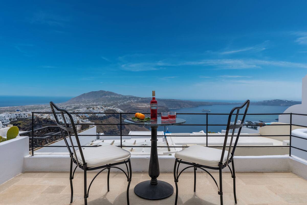 Un balcon avec une table et deux chaises, offrant une vue panoramique sur la côte et les montagnes.