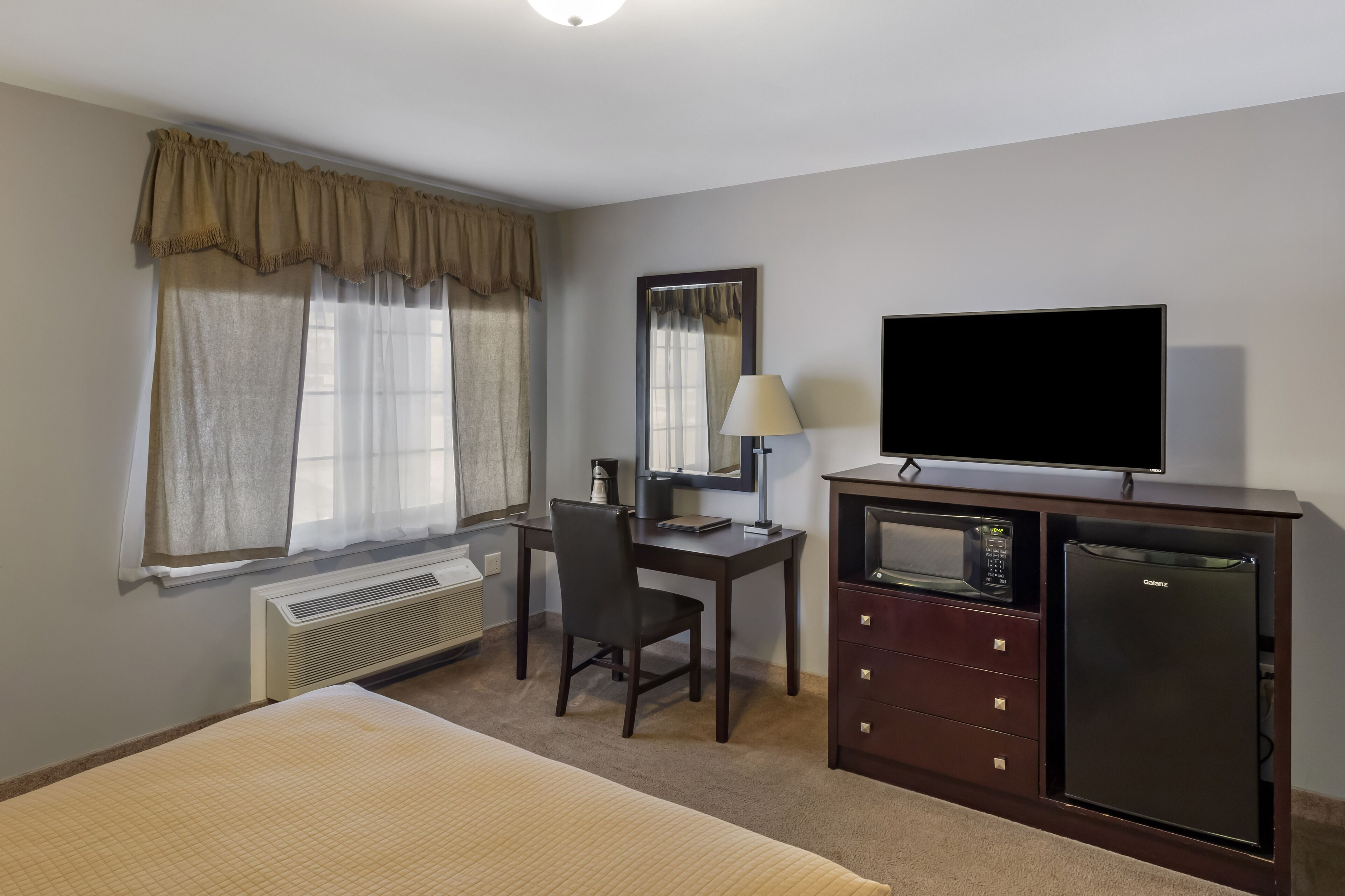 Habitación de hotel con cama, escritorio, silla, televisor, microondas y refrigerador.