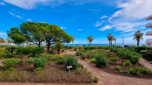 A landscaped garden with various plants and trees, a pathway, and a view of the sea and buildings in the background. - Apartment 4 guests with access to the beach/Fr éjus (Fréjus)