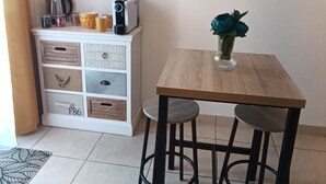 Un coin repas avec une table en bois et deux tabourets, un meuble blanc avec des tiroirs de rangement et des étagères décoratives murales.