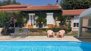 Une piscine avec des chaises longues et une maison dotée d’un toit en tuiles et de plantes en pot.