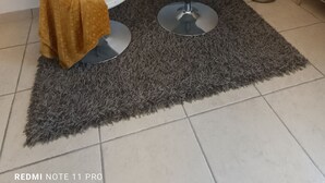 Un salon moderne avec deux fauteuils blancs, un tapis gris, un grand vase contenant des plantes séchées et un tableau accroché au mur.