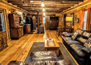 L’intérieur d’un chalet rustique est doté d’un plancher en bois, d’un canapé en cuir, d’une table à manger et d’un coin cuisine avec des armoires en bois et un réfrigérateur.