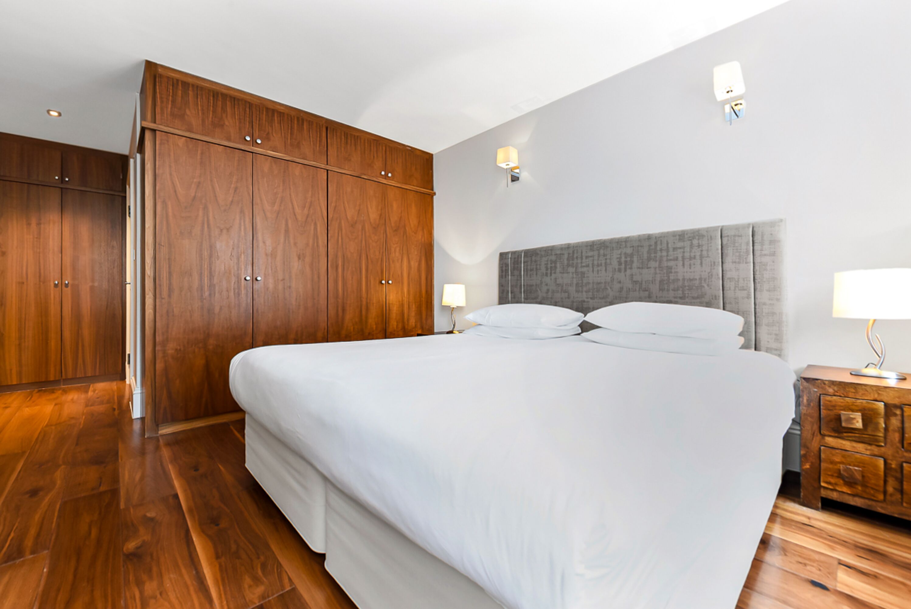 Une chambre à coucher avec un grand lit, une armoire en bois et une table de chevet avec une lampe.