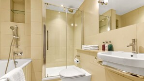 Ein modernes Badezimmer mit einer Duschkabine, einer weißen Badewanne, einer Toilette und einem Waschbecken mit Pflegeprodukten.