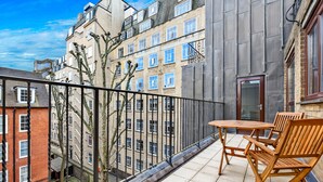 Ein Balkon mit Tisch und Stühlen, mit Blick auf eine Stadtlandschaft mit mehreren Gebäuden.