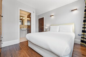 A modern hotel room with a large bed, a bathroom with a mirror, and a wooden floor.