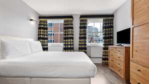 Ein Hotelzimmer mit Bett, Fernseher, einem Holzschrank und einem Fenster mit Vorhängen.