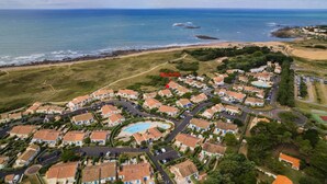 Vue aérienne d’un quartier résidentiel situé sur la côte, avec des maisons, une piscine et une plage.