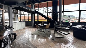 Una habitación amplia con un ventanal grande, una escalera, una zona de comedor y una motocicleta.