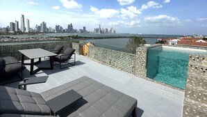 Terraza en la azotea con piscina, zona de estar y vista panorámica de un horizonte urbano sobre un cuerpo de agua.