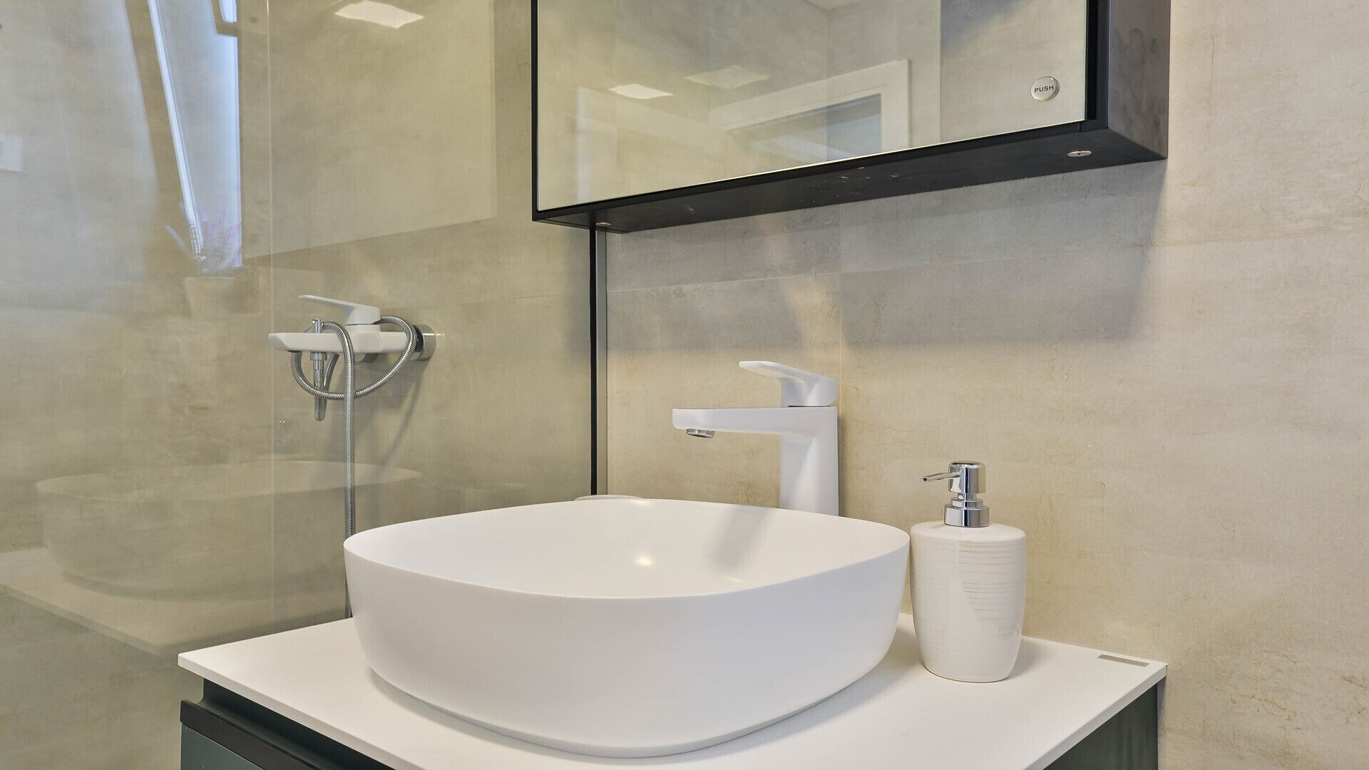 Ein modernes Badezimmer mit einem großen, runden weißen Waschbecken, einer Duschbrause und einem Seifenspender.