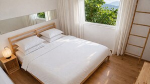 A neatly made bed with white linens, a wooden headboard, a bedside lamp, and a view of greenery through a window. - Grand Seaview Retreat - walk to the beach (Thessaloniki)