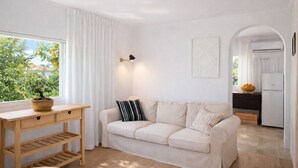 A living room with a sofa, a wooden table, a potted plant, and a view of the outside. - Grand Seaview Retreat - walk to the beach (Thessaloniki)