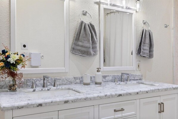 Une salle de bain avec un lavabo en marbre blanc, deux robinets, un miroir et deux serviettes suspendues à des porte-serviettes.