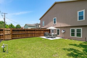 A backyard with a wooden fence, a grill, and a patio with outdoor furniture. - Get Together & Stay-Play-Relax! Peaceful Oasis w/ TVs, Games, & BBQ -LUCKY House (Houston)