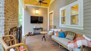 A covered porch with a wooden ceiling, a TV mounted on the wall, wicker furniture, and a brick wall. - Spacious Midway Cottage w/ Porches, Near Hunting! (Midway)