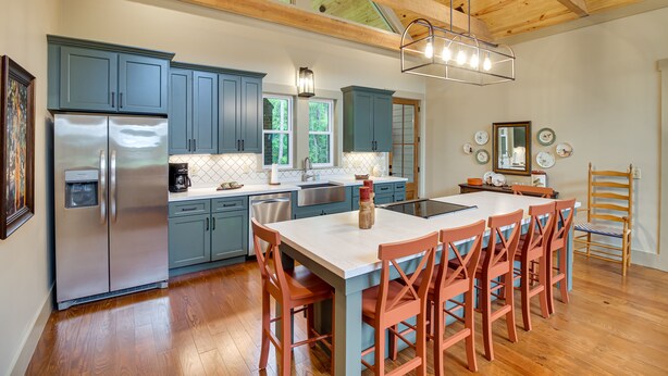 A modern kitchen with blue cabinets, a stainless steel refrigerator, and a large island with red chairs. - Spacious Midway Cottage w/ Porches, Near Hunting! (Midway)
