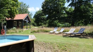 A pool area with a wooden deck, a small building with a red roof, and three lounge chairs in the background.
