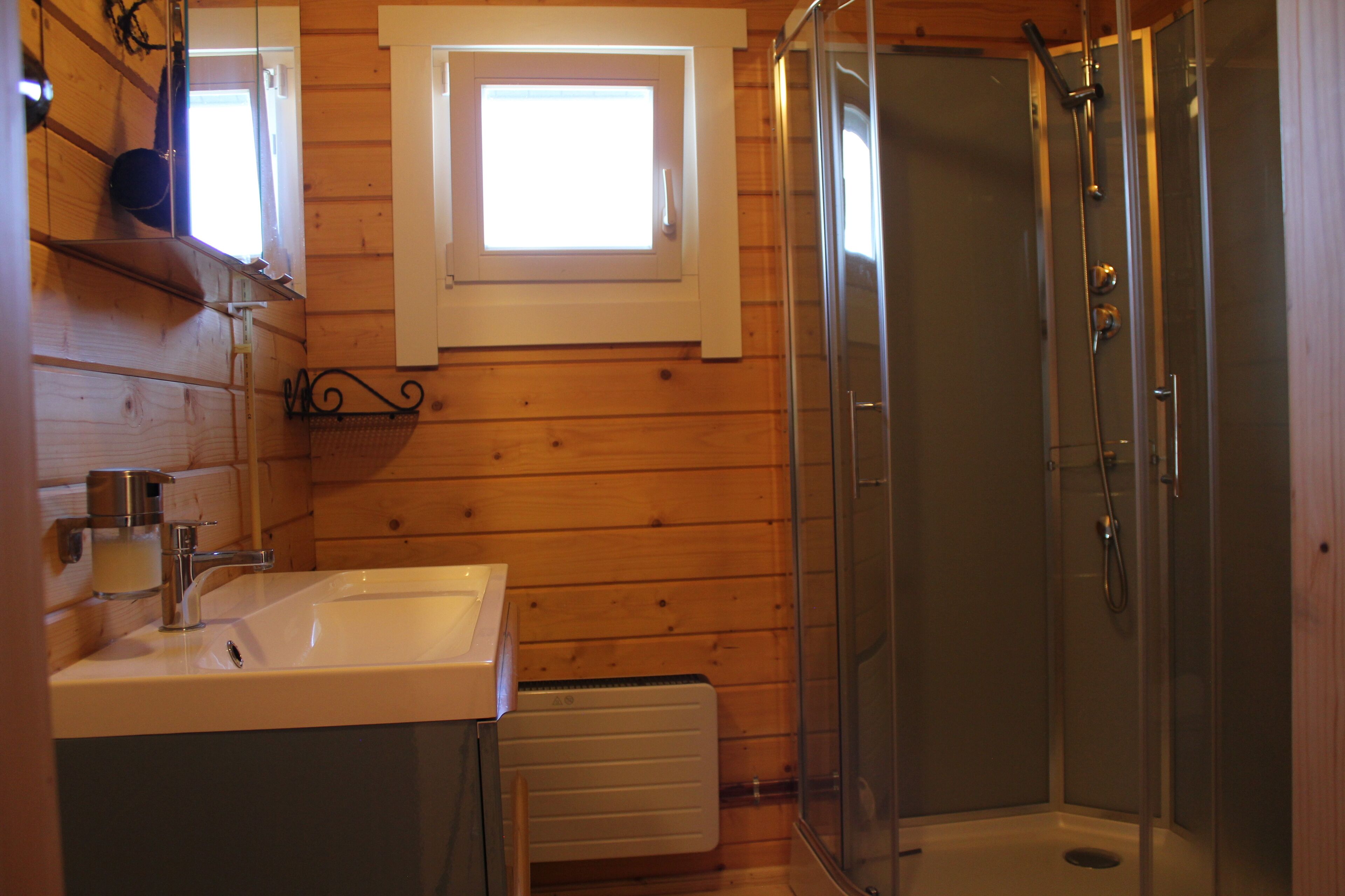 A bathroom with a wooden interior, a sink, a window, and a glass-enclosed shower.