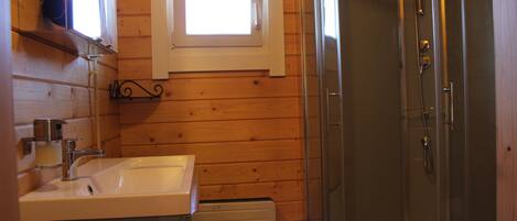 A bathroom with a wooden interior, a sink, a window, and a glass-enclosed shower.