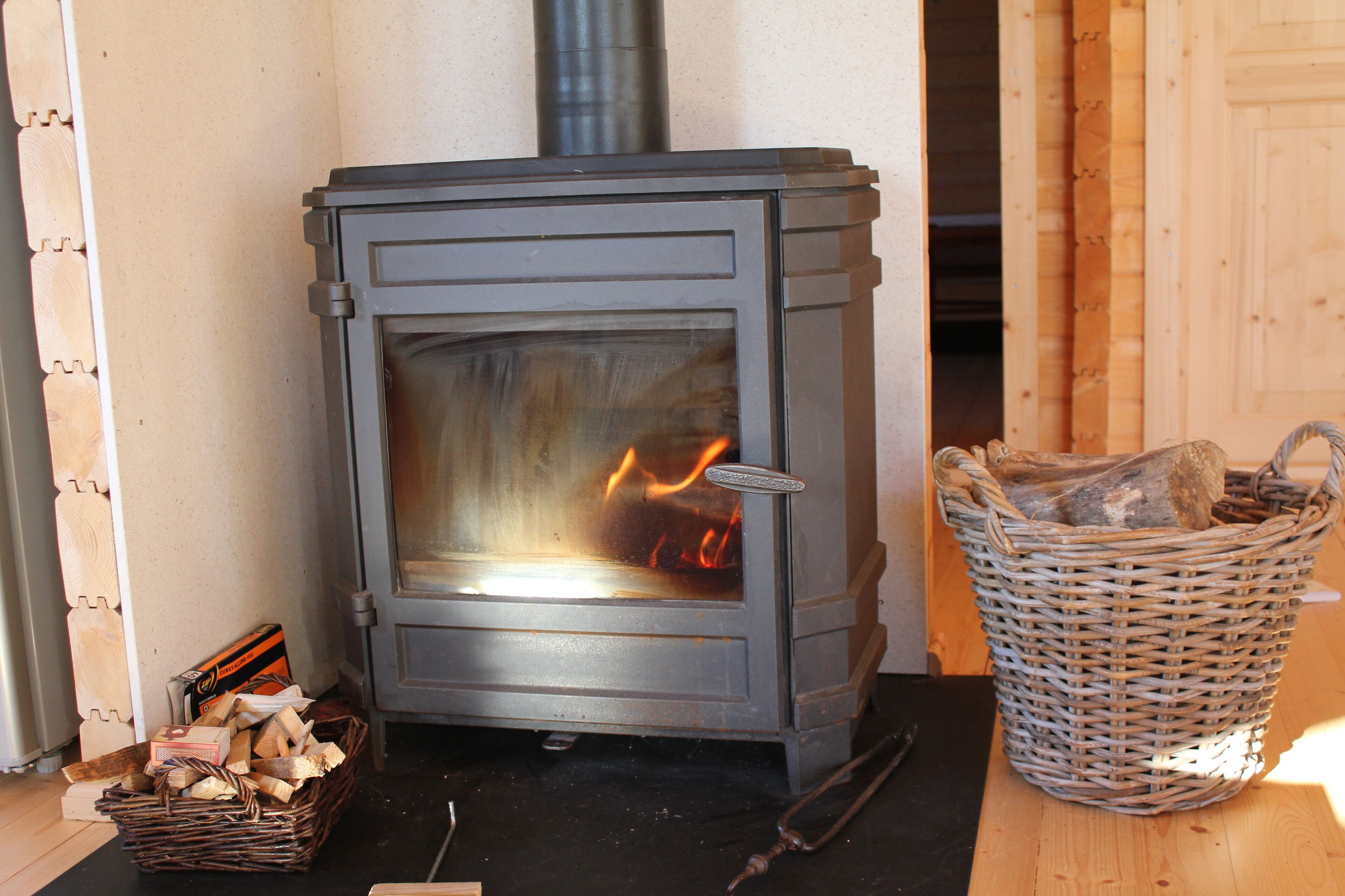 Un poêle à bois, avec un panier de bois de chauffage à côté.