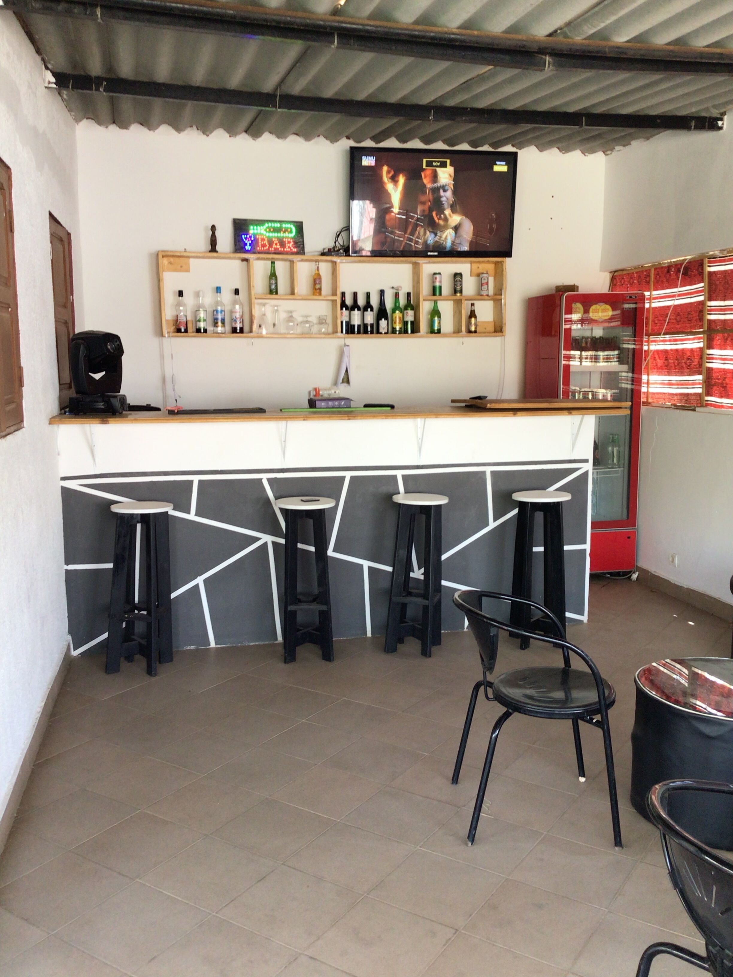 Zona de bar con mostrador, taburetes y una pantalla de televisión que muestra un programa.