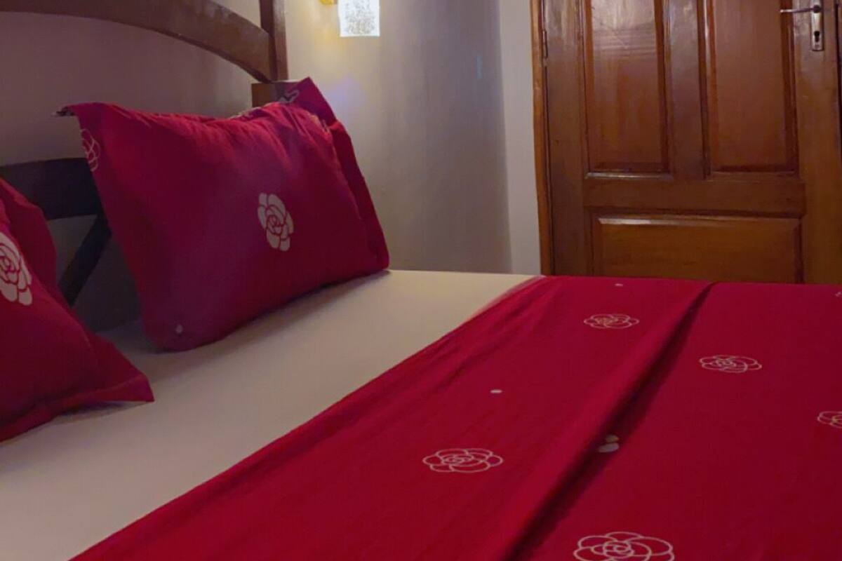 A bedroom with a wooden door, a bed with red bedding, and a wall decoration.