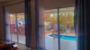 A room with a large sliding glass door leading to an outdoor pool area. - Black And White Hôtel (Toubab Dialao)
