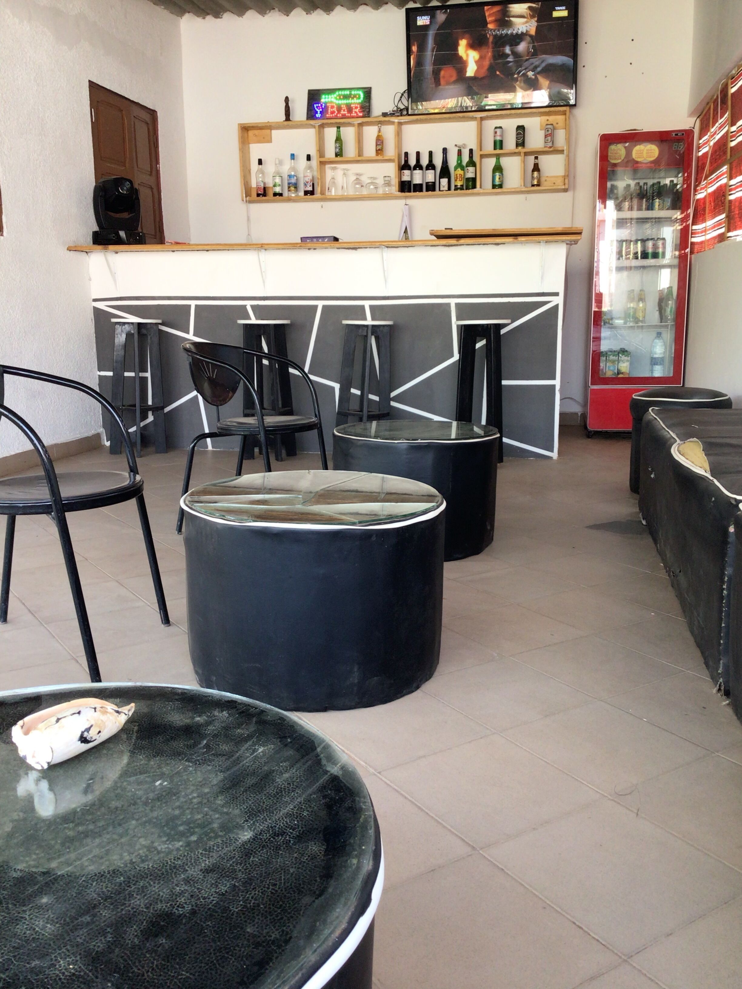 A bar area with stools, a counter with bottles, and a television screen.
