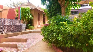 A courtyard with a thatched-roof hut, a tiled wall, and a variety of plants.