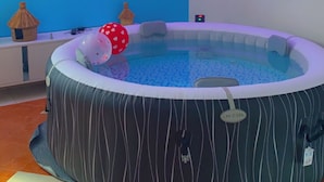 A room with a large, striped, circular hot tub, a flat-screen TV mounted on the wall, and a decorative sunburst light fixture.