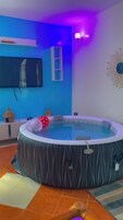 Una habitación con un jacuzzi circular grande y a rayas, un televisor de pantalla plana montado en la pared, y un aplique decorativo con forma de sol.