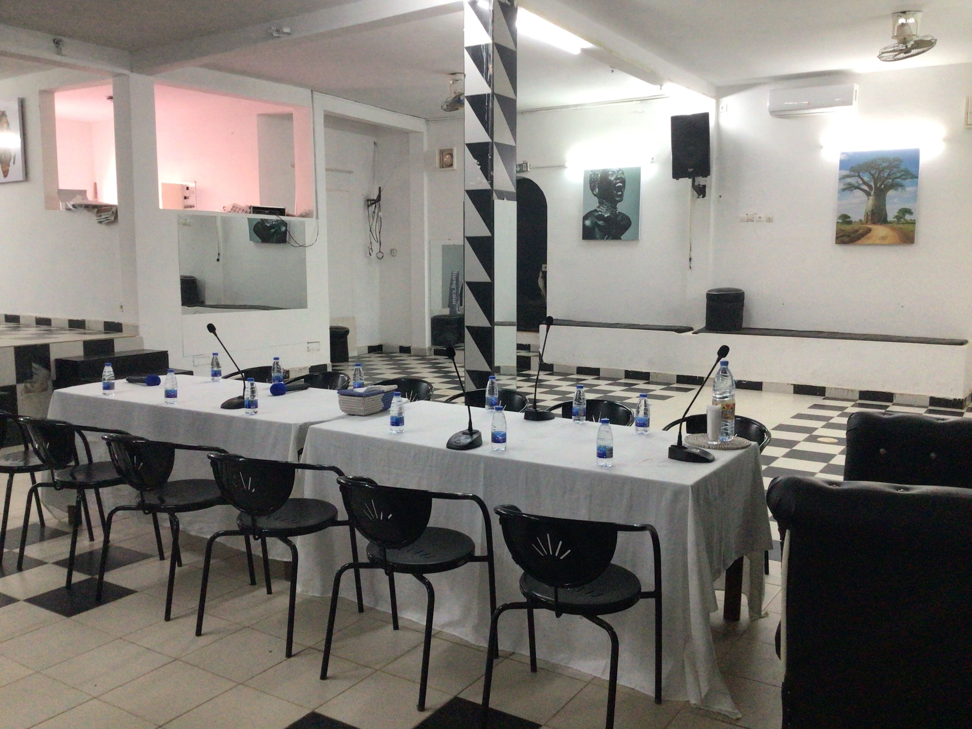 Un salón de conferencias con mesas, sillas, una escalera y obras de arte en las paredes.