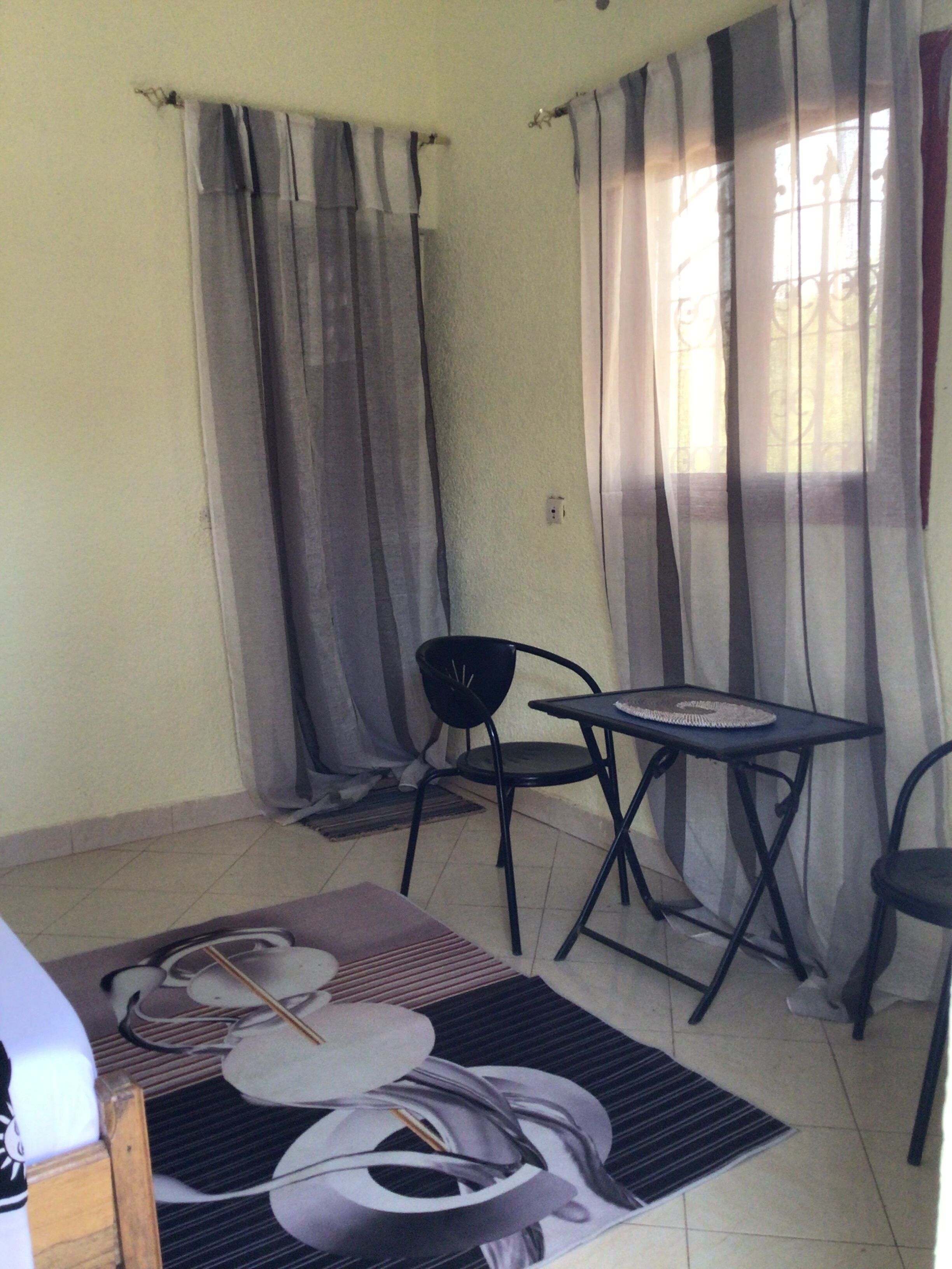 A small room with a table and two chairs, a window with curtains, and a tiled floor.