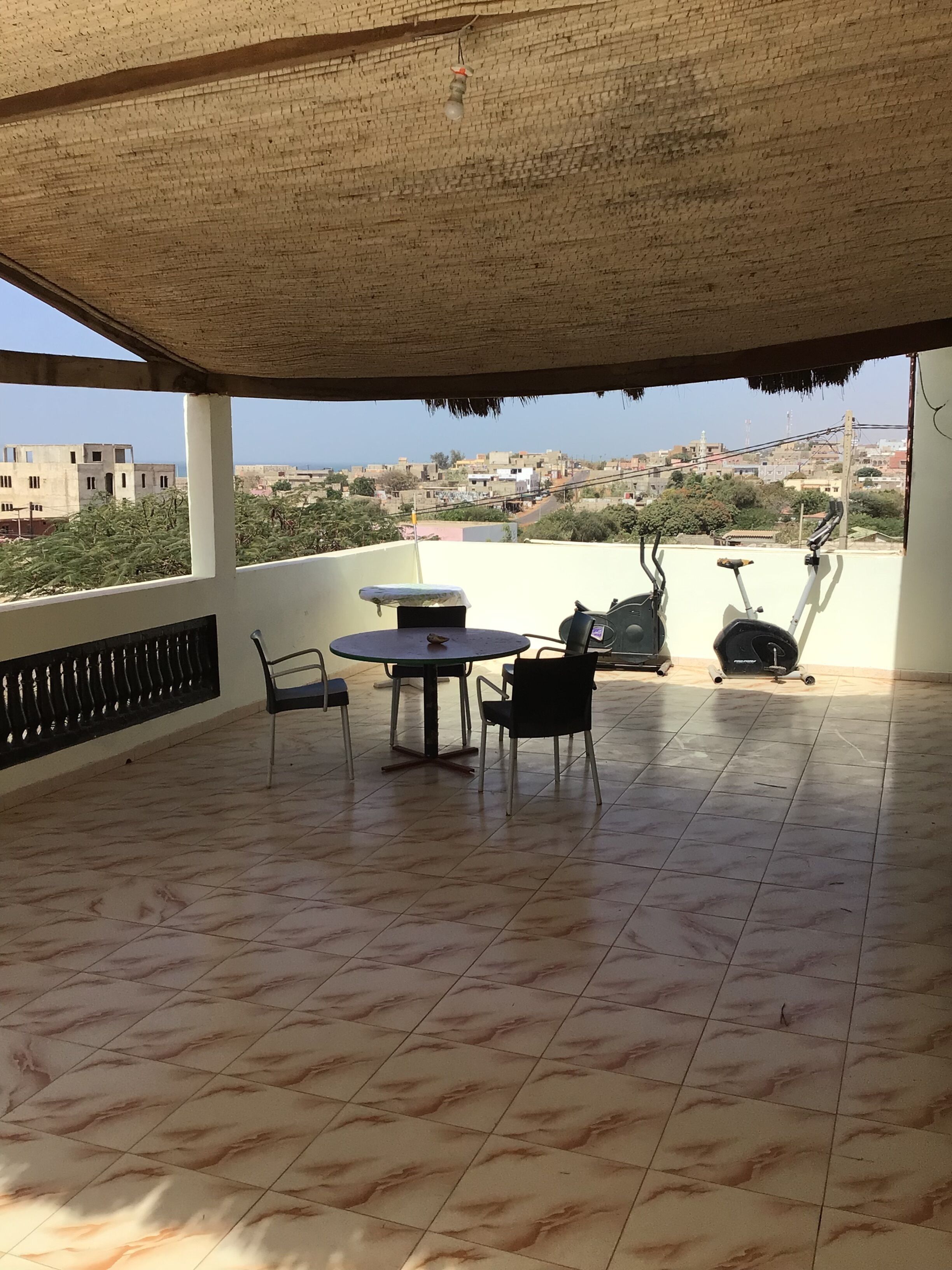 A covered outdoor area with a table and chairs, a ceiling fan, and a view of a cityscape in the background.
