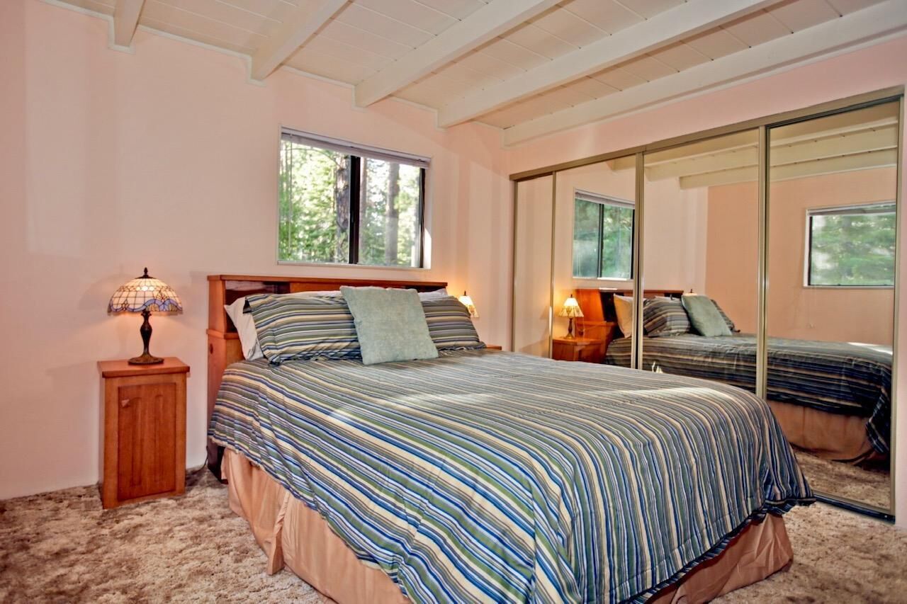 A bedroom with a large bed, a nightstand, a lamp, a mirror, and a window.