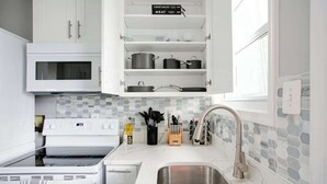 Una cucina moderna con mobili bianchi, un microonde integrato, un lavello in acciaio inossidabile e uno schienale piastrellato.