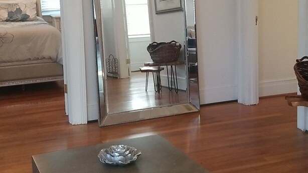 A spacious living room with a large mirror, a wooden coffee table, and a dining area visible through the mirror.