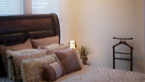 A bedroom with a bed, bedside lamps, a hanging plant, and a wardrobe.