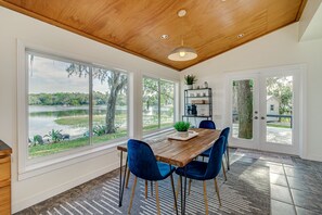 Un comedor con mesa de madera, sillas azules y vista a un lago a través de amplios ventanales.