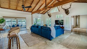 A spacious living room with a blue sectional sofa, a ceiling fan, and a mounted deer head. - Cozy Cottage on Crooked Lake (Babson Park)