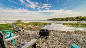 A lakeside patio with Adirondack chairs, a fire pit, and a view of the lake and distant trees. - Cozy Cottage on Crooked Lake (Babson Park)