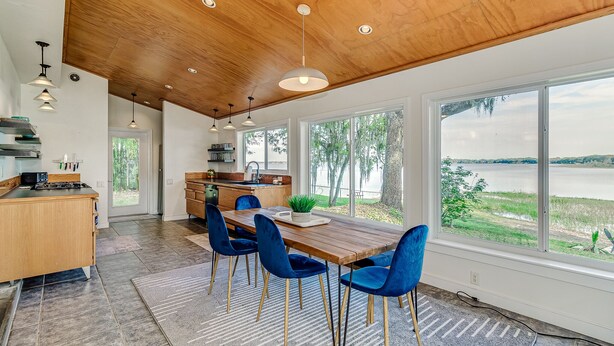 A modern kitchen with a wooden ceiling, large windows, and a dining area with blue chairs. - Cozy Cottage on Crooked Lake (Babson Park)