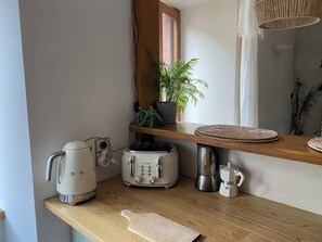 A kitchen with a coffee maker, toaster, kettle, and a potted plant on a wooden shelf.