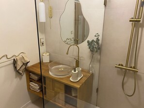 Une salle de bain moderne dotĂ©e dâune douche Ă parois de verre, dâun meuble-lavabo en bois avec un vasque en verre, et dâun miroir Ă la forme originale.