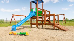 Eine hölzerne Spielanlage mit Rutsche und Schaukeln auf Sand.