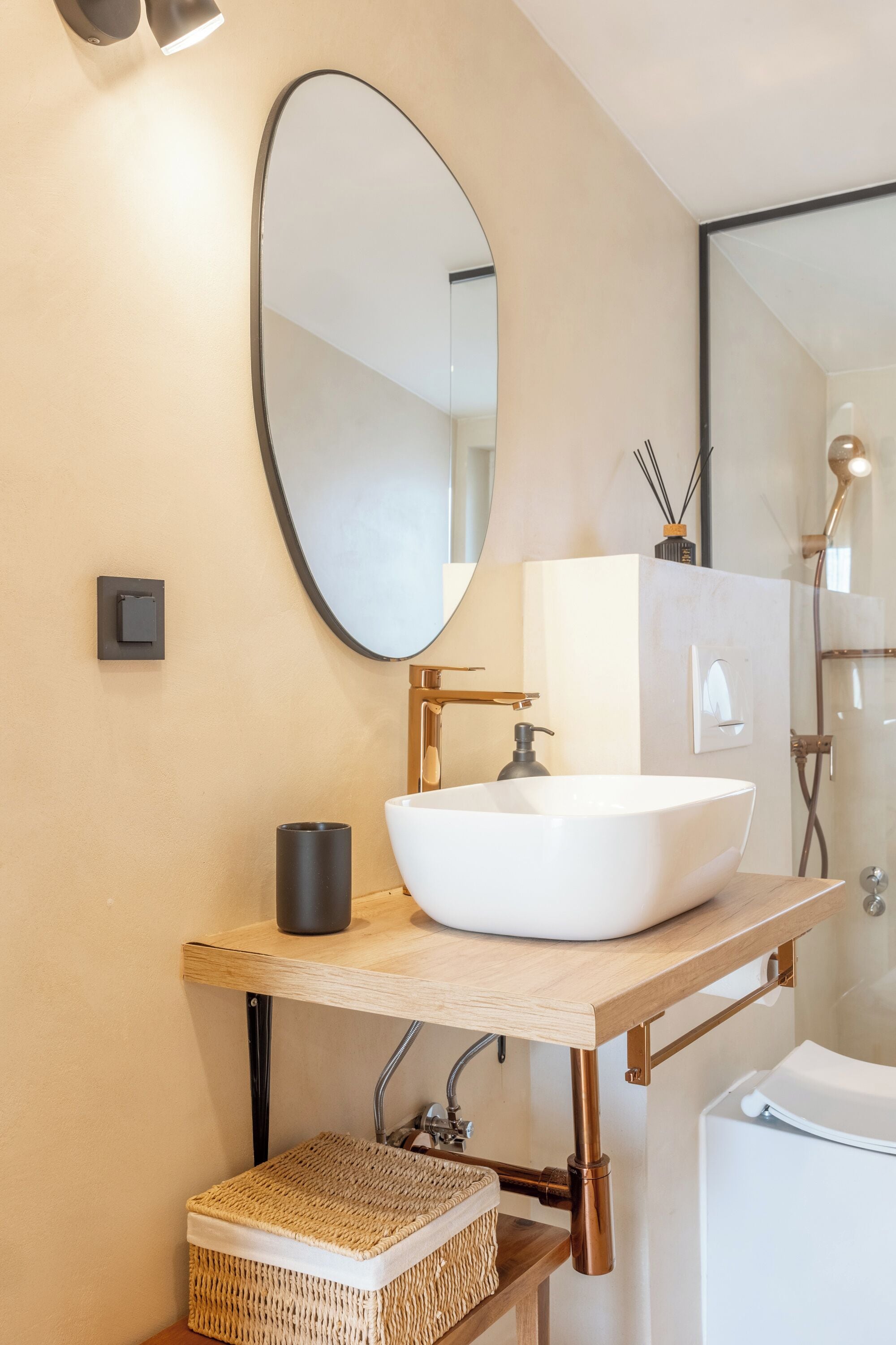 Een moderne badkamer met een witte wastafel, een grote ovale spiegel en een douchecabine.
