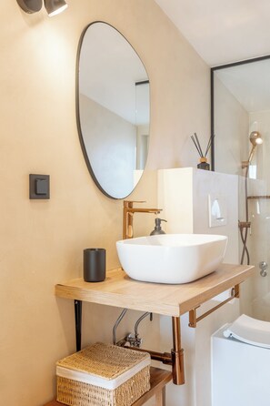 Ein modernes Badezimmer mit einem weißen Waschbecken, einem großen, ovalen Spiegel und einer Duschkabine.