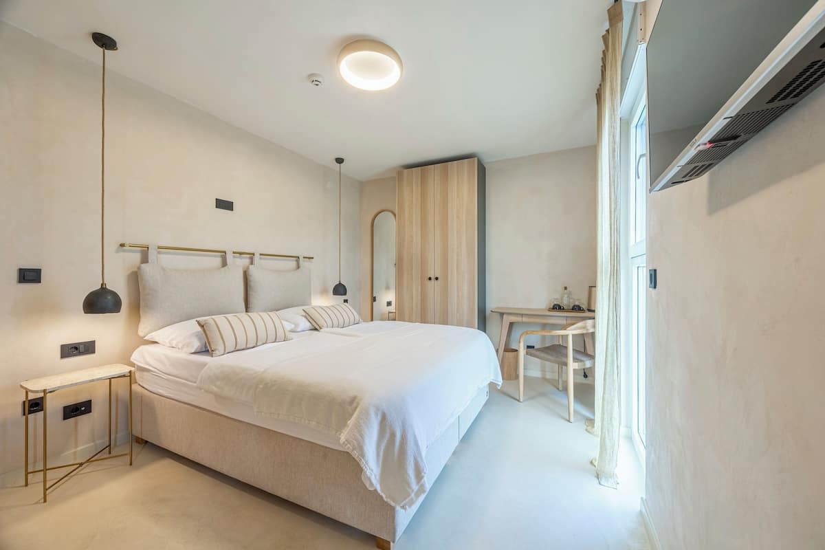 A modern bedroom with a large bed, bedside tables, a desk, and a wardrobe.